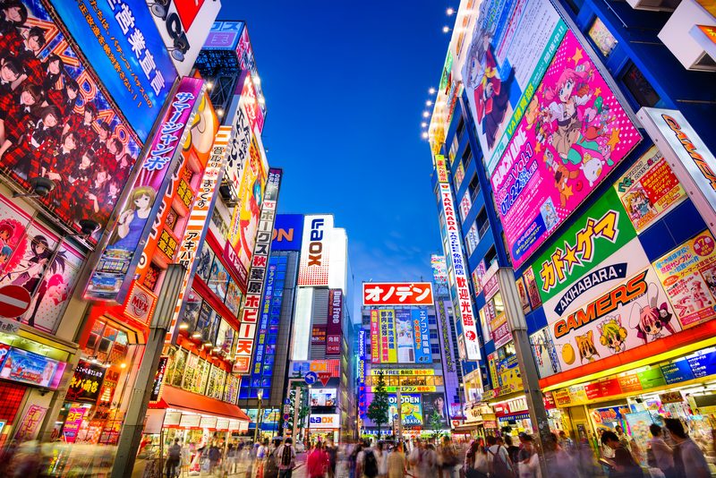 Crowds walking beneath bright neon signs in Tokyo at dusk